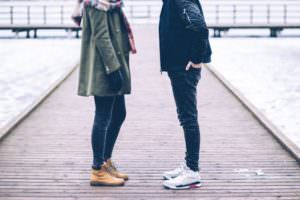 Couple standing face to face on a wooden pier, a gap between them